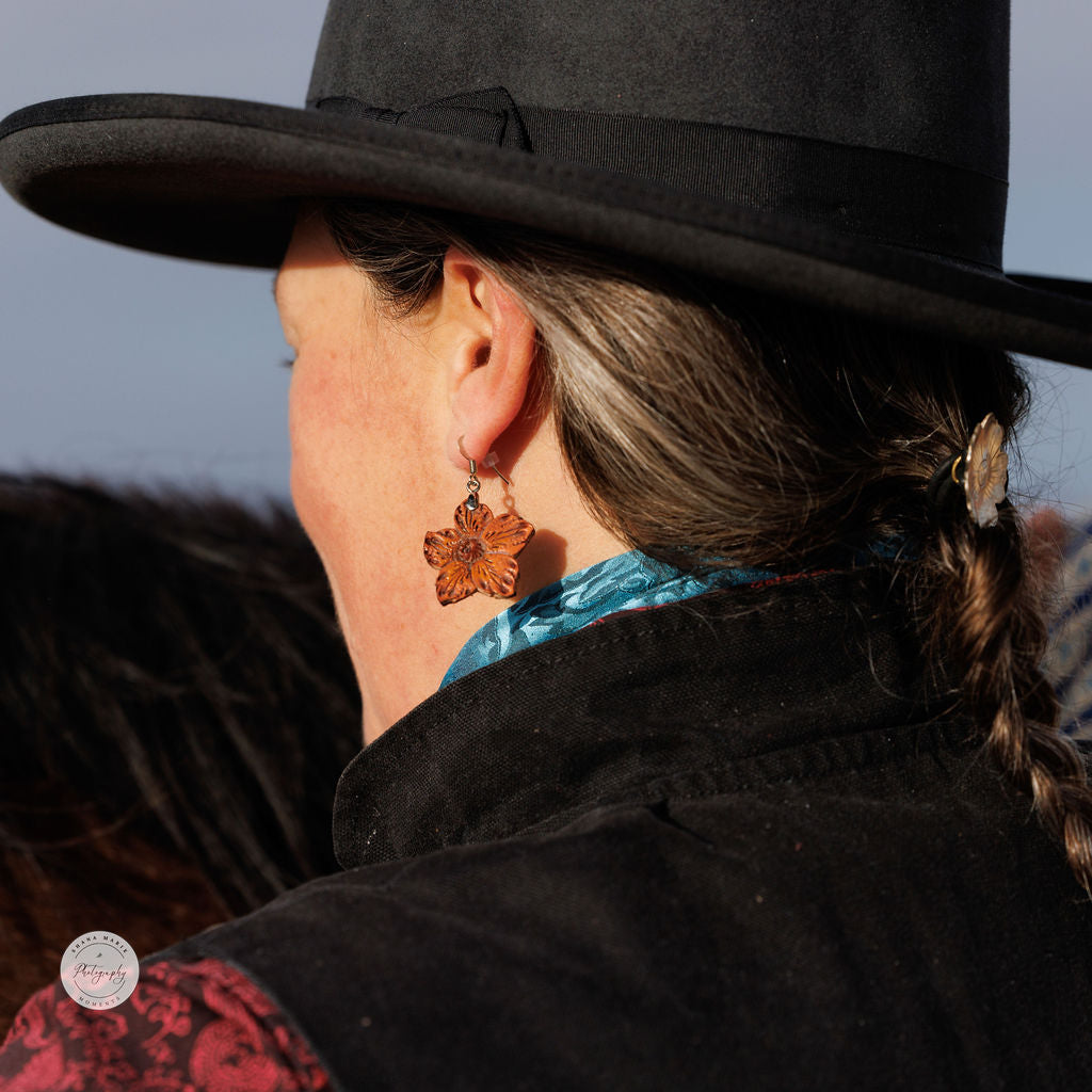 Cowgirl wearing a leather earring while standing next to a horse