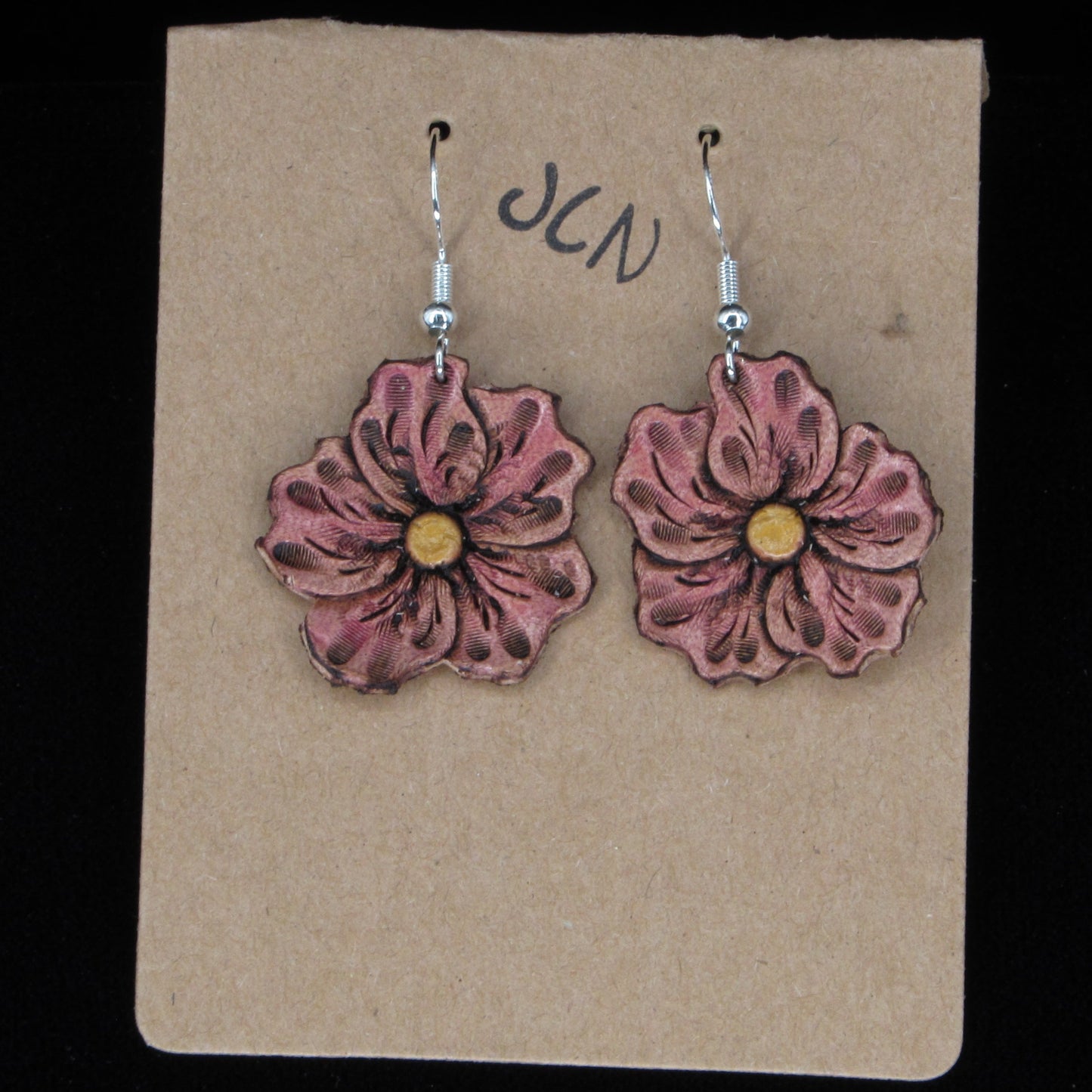 Flower-shaped earrings on a beige card with 'JLN' branding against a black background