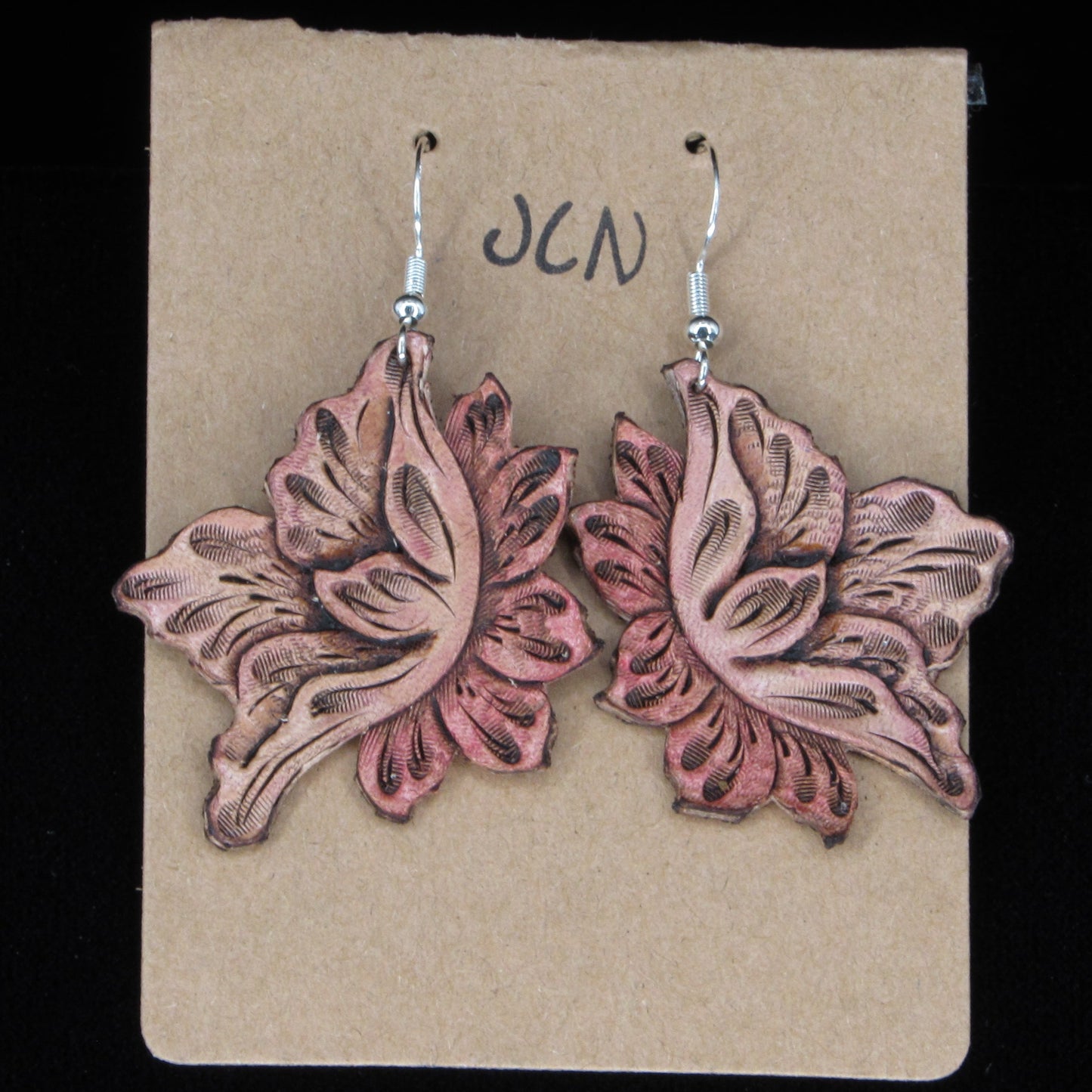 Flower-shaped leather earrings on a brown card with 'JLN' branding against a black background