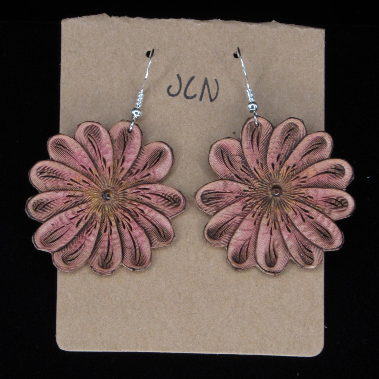 Flower-shaped leather earrings on a brown card with 'JLN' branding against a black background