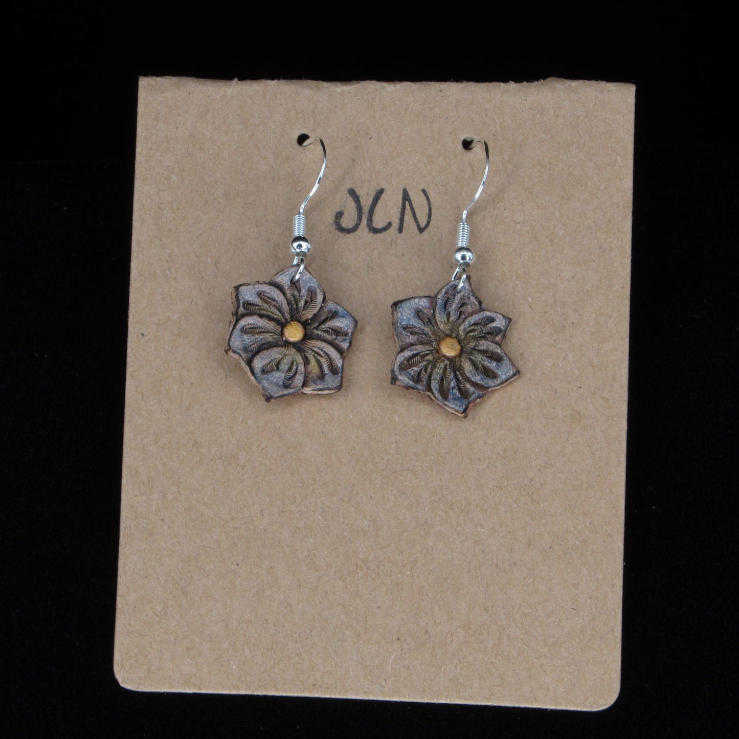 Flower-shaped earrings on a brown card with 'JLN' branding against a black background