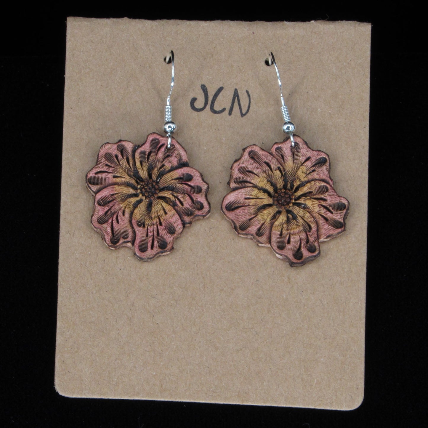 Flower-shaped leather earrings on a brown card with 'JLN' branding against a black background