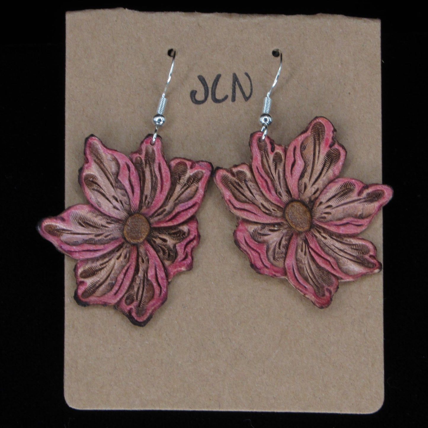 Flower-shaped leather earrings on a brown card with 'JLN' branding against a black background