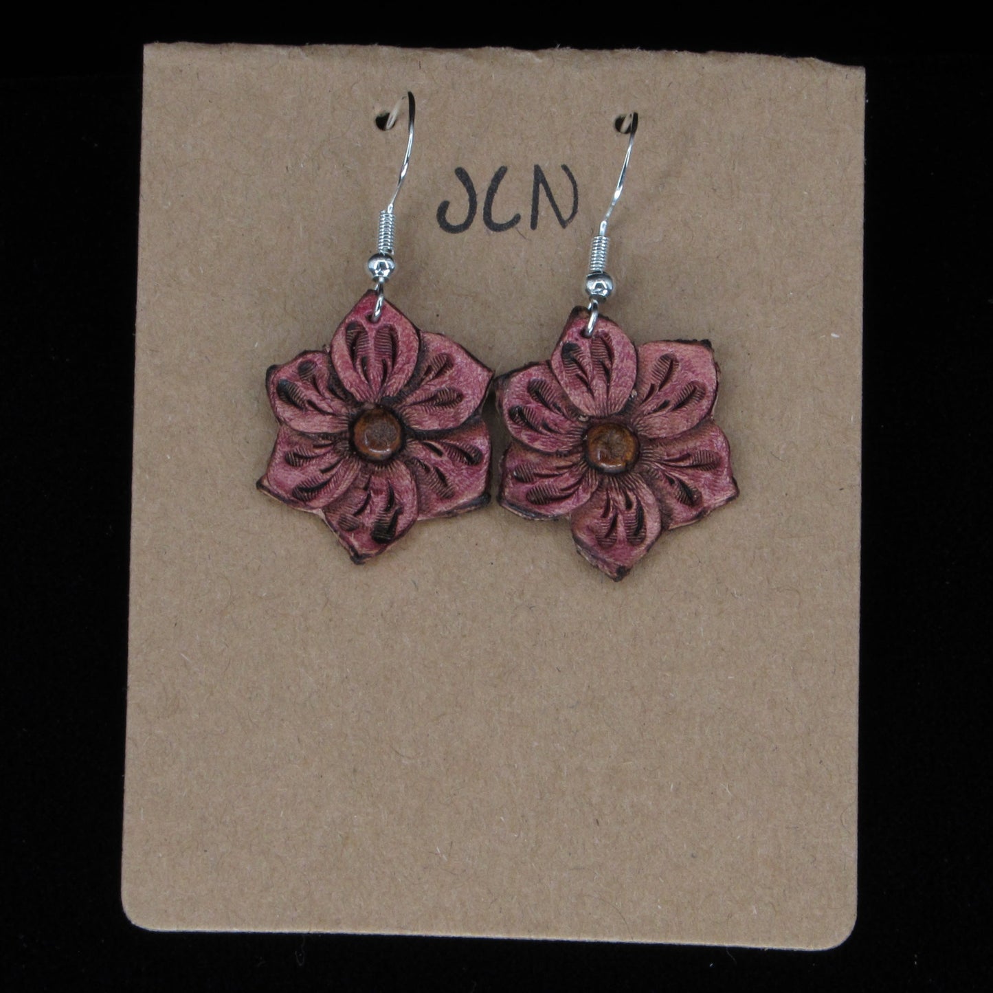 Pink flower-shaped earrings on a beige card with 'JLN' branding against a black background