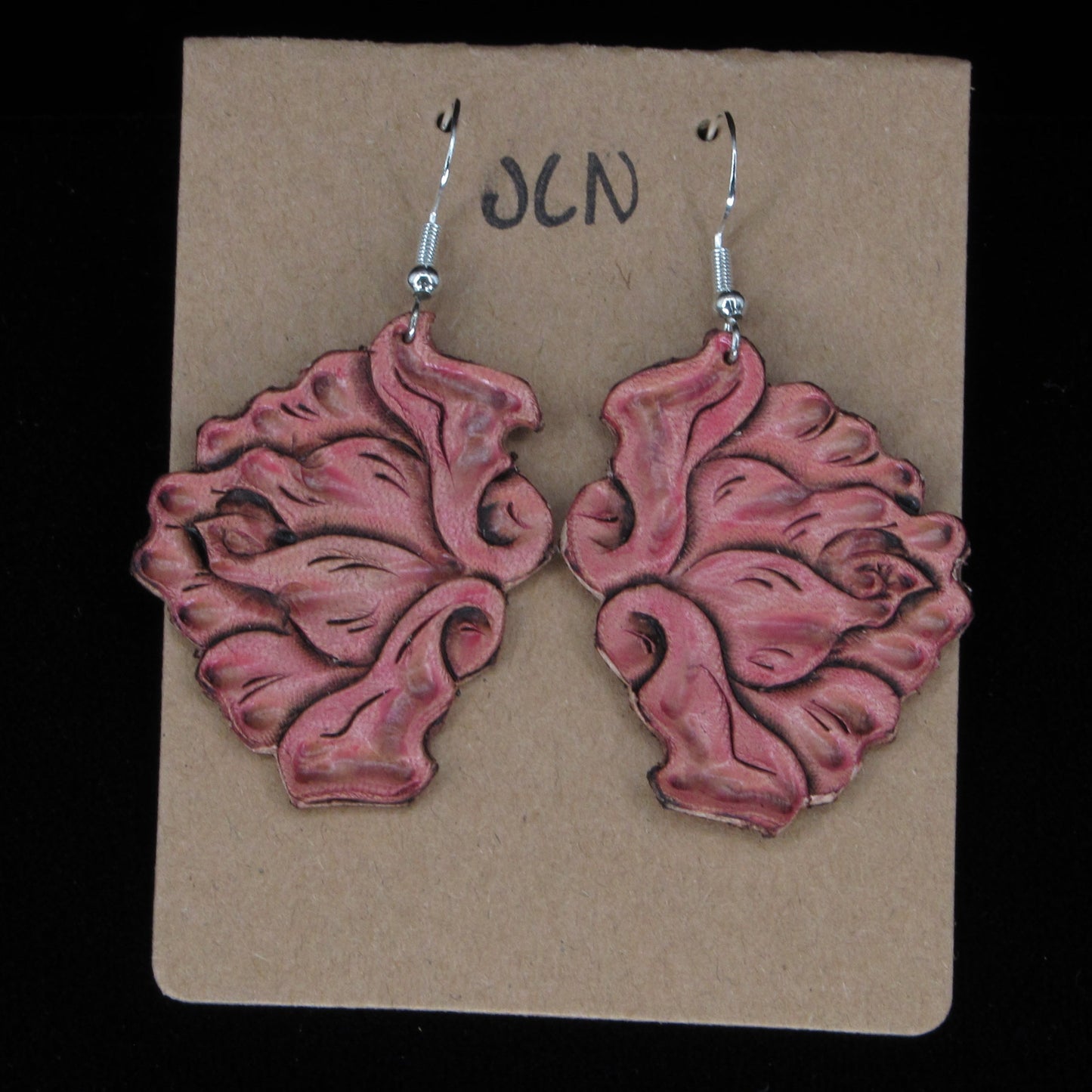 Pink flower-shaped earrings on a beige card with 'JLN' branding against a black background