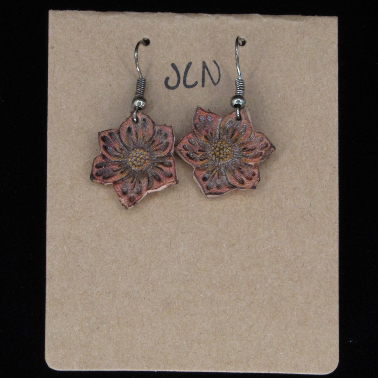 Flower-shaped earrings on a beige card with 'JLN' branding against a black background