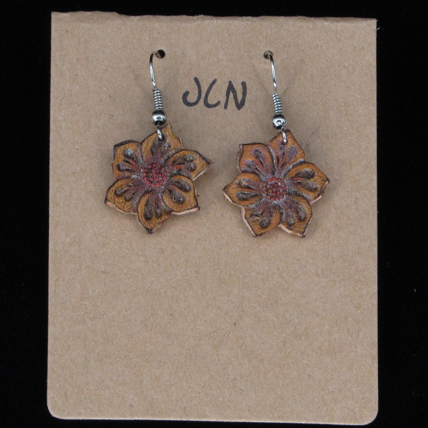 Flower-shaped earrings on a beige card with 'JLN' branding against a black background
