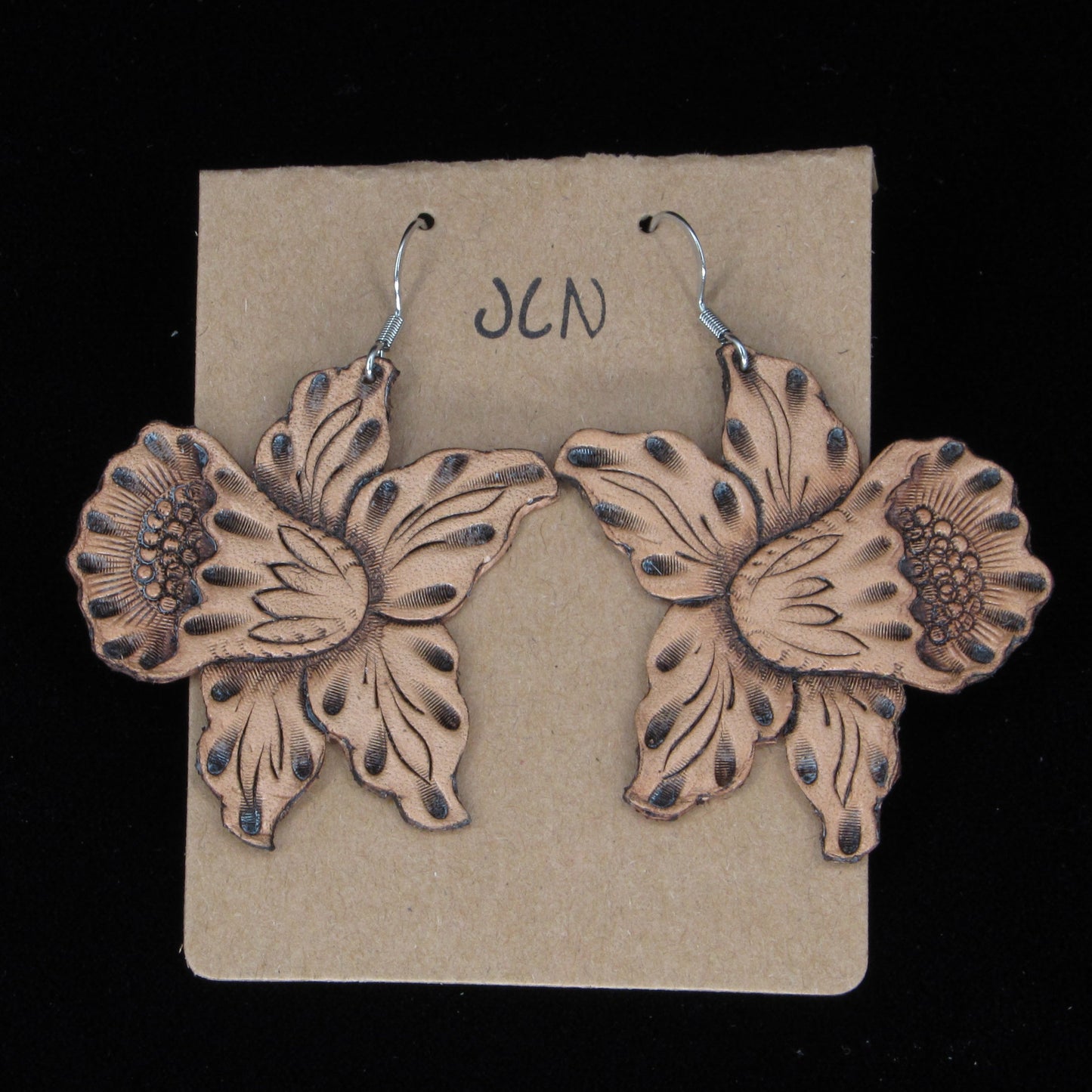 Flower-shaped earrings on a beige card with 'JLN' branding against a black background