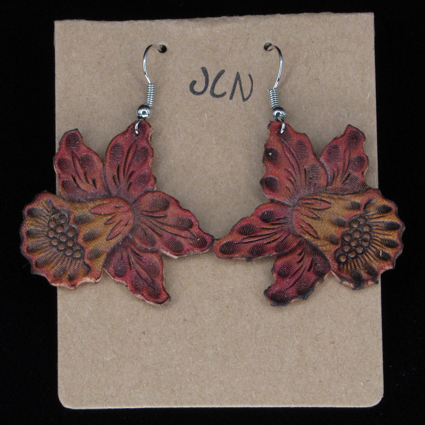 Flower-shaped earrings on a beige card with 'JLN' branding against a black background