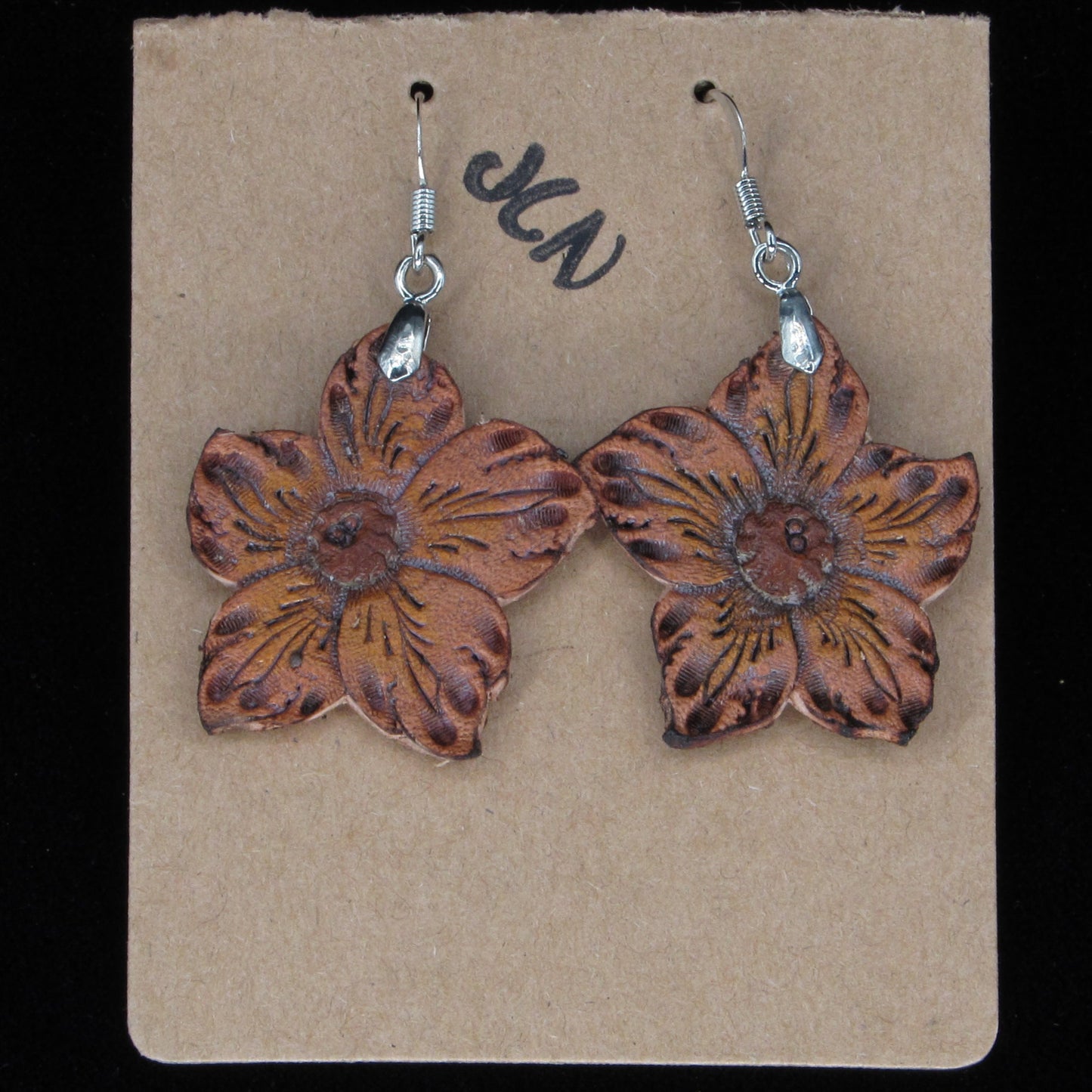 Flower-shaped earrings on a beige card with 'JLN' branding against a black background