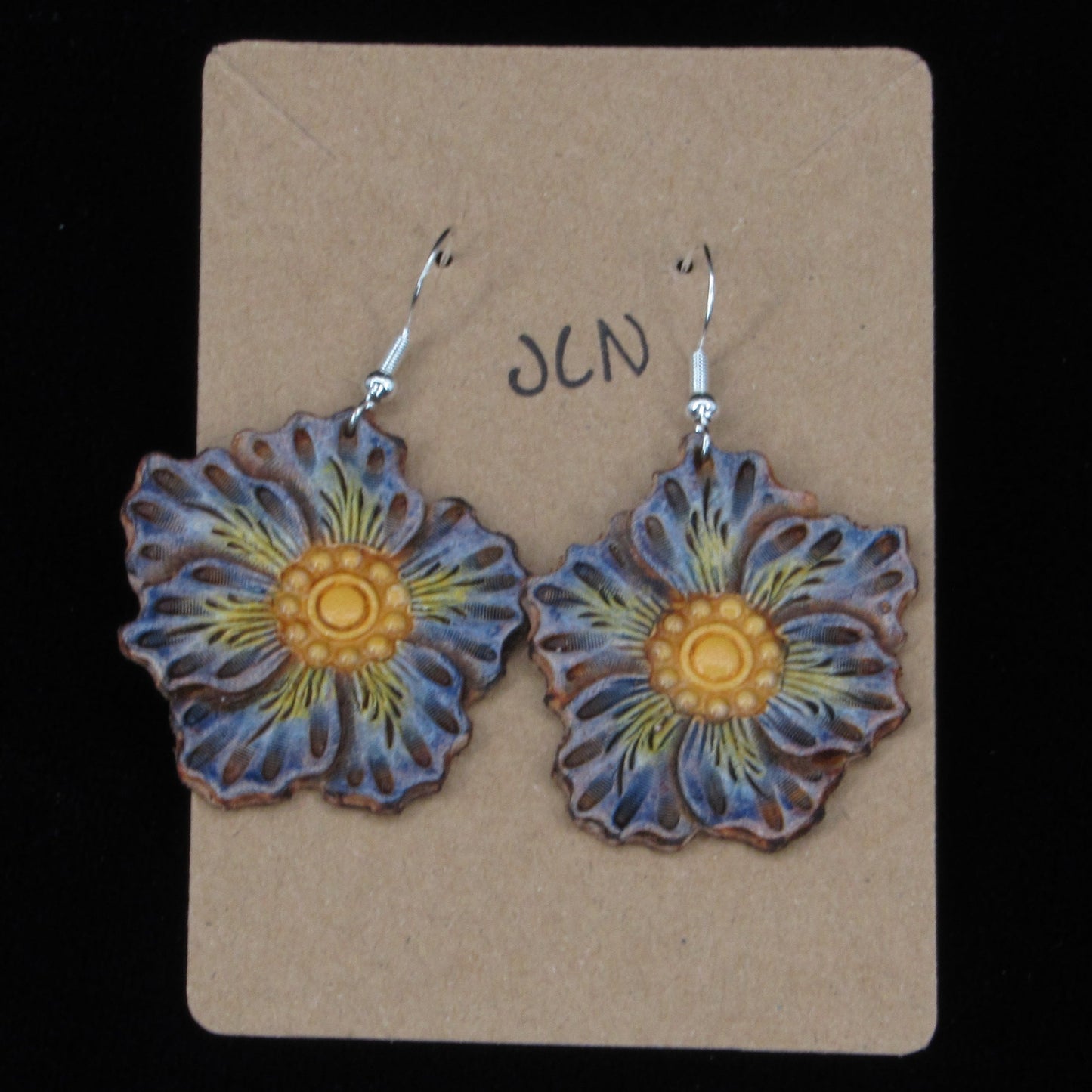 flower shaped leather earrings on a tan card against a black background