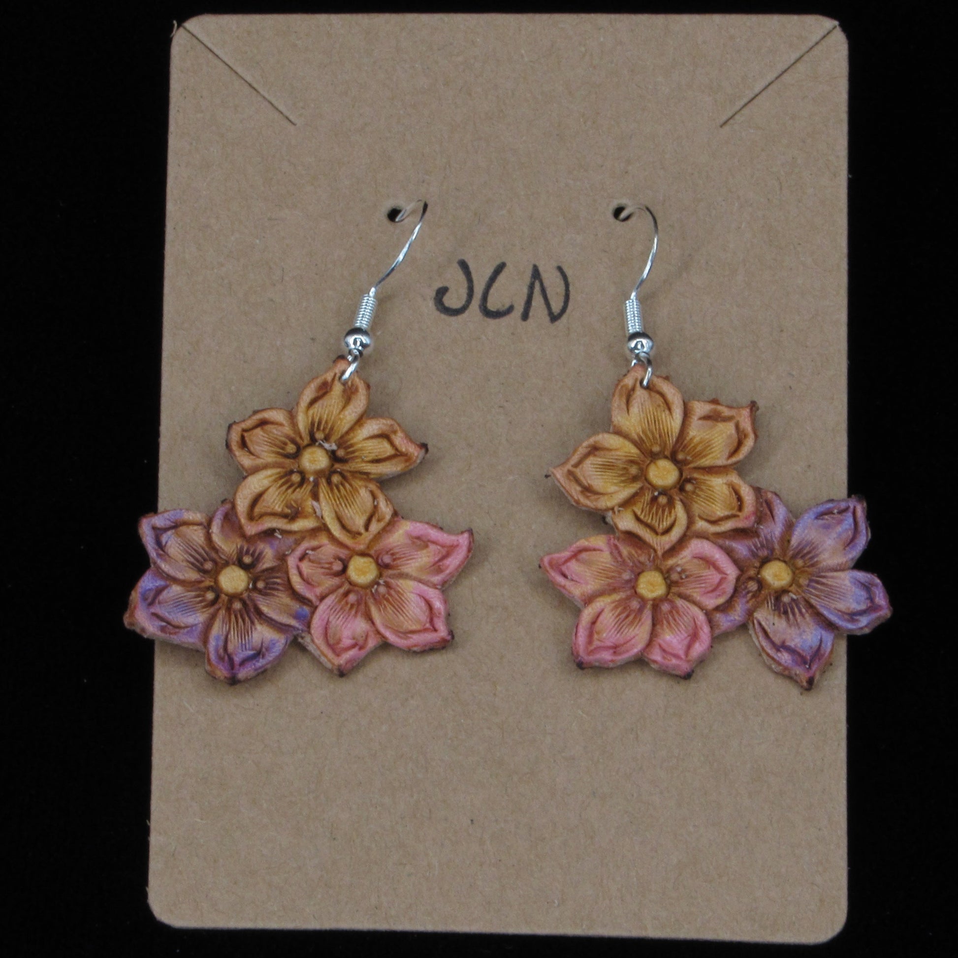 flower shaped leather earrings on a tan card against a black background