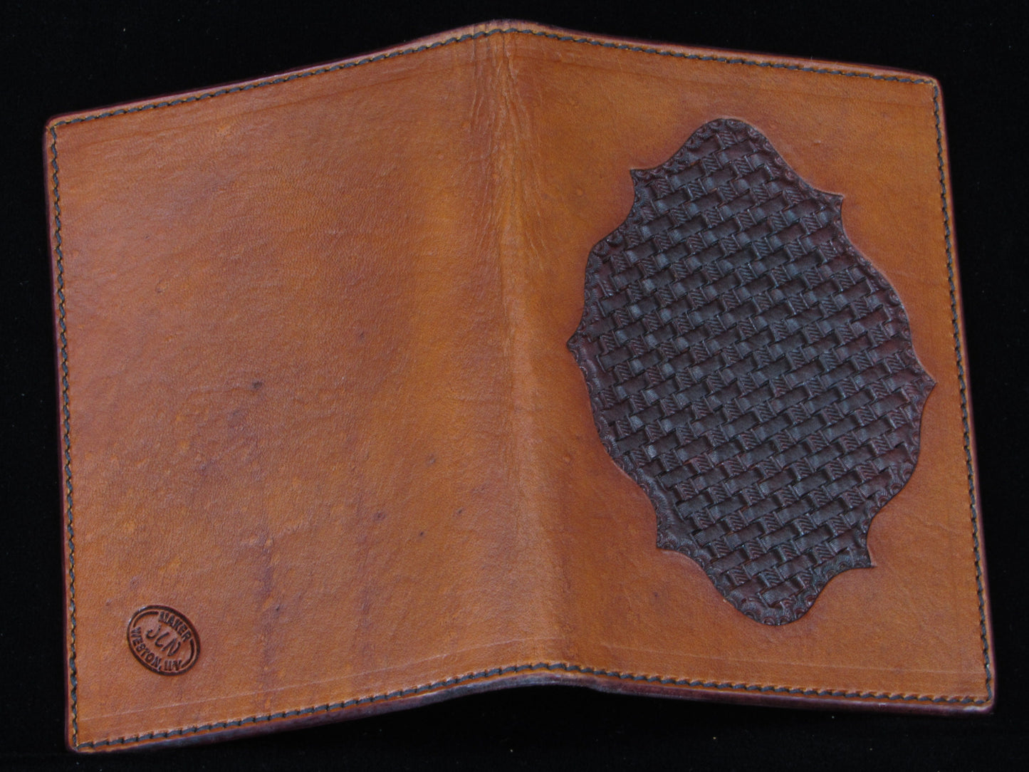 Brown leather passport wallet with a basket stamped inset. on a black background