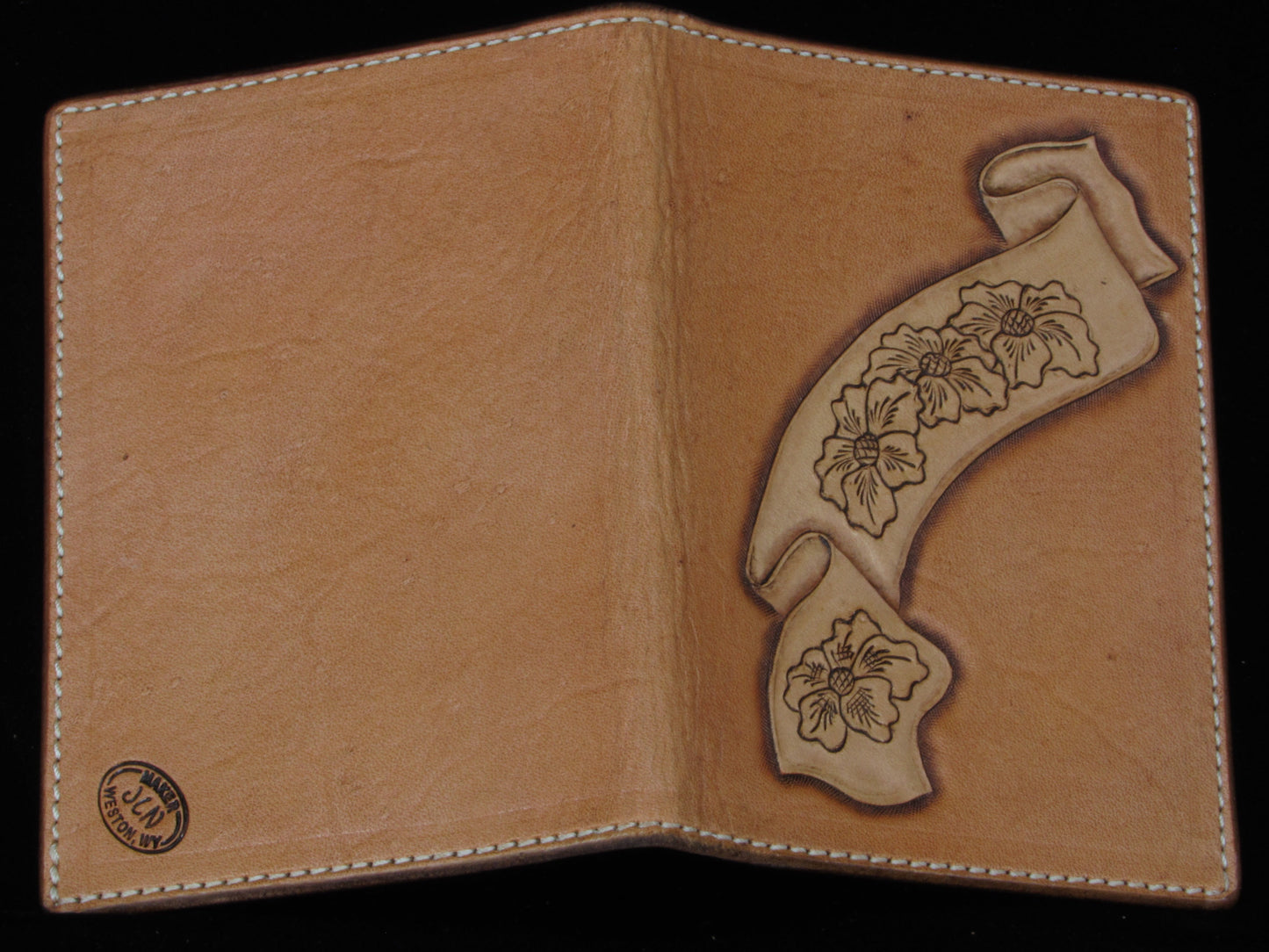 Tan leather passport wallet with floral designs on a black background