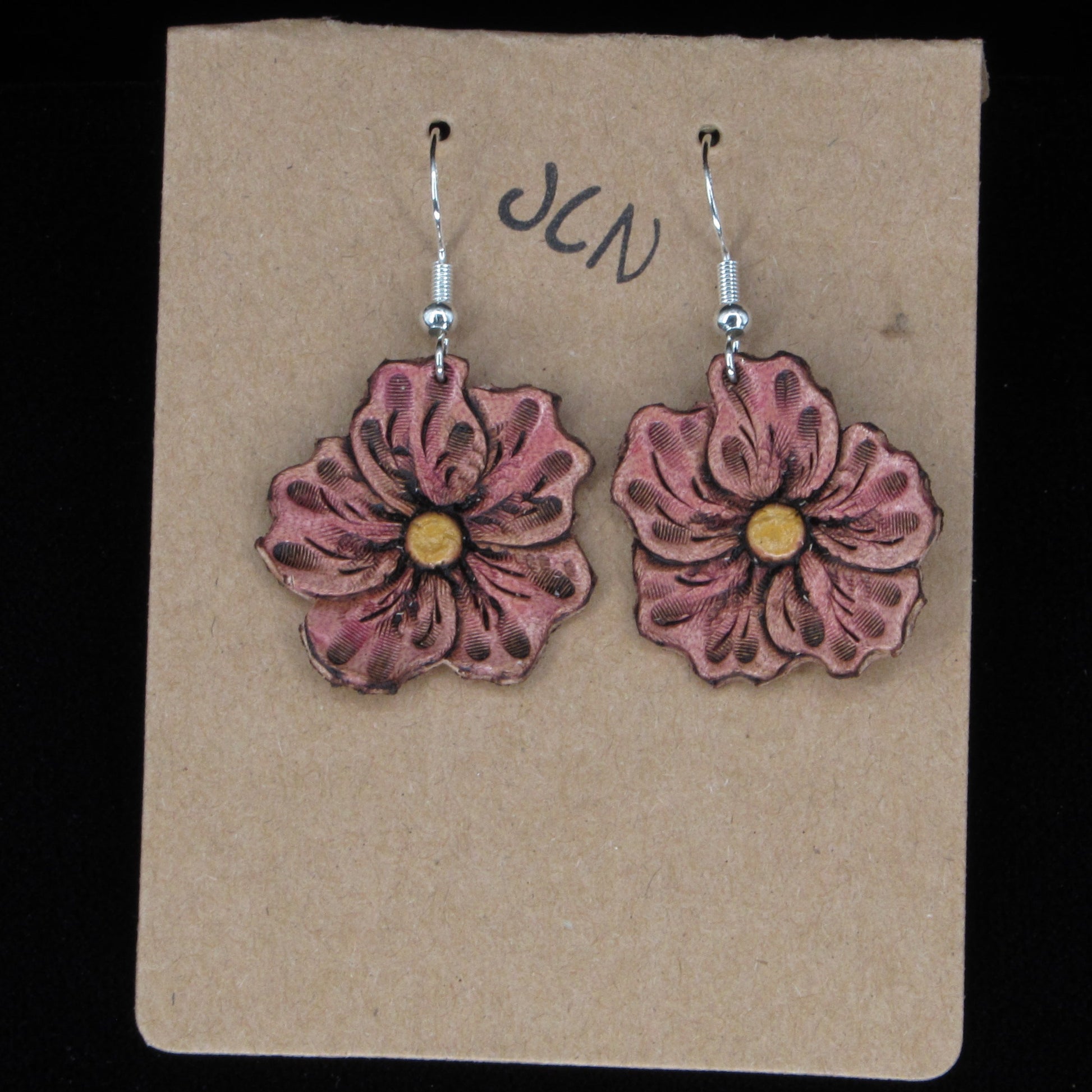 Flower-shaped earrings on a beige card with 'JLN' branding against a black background