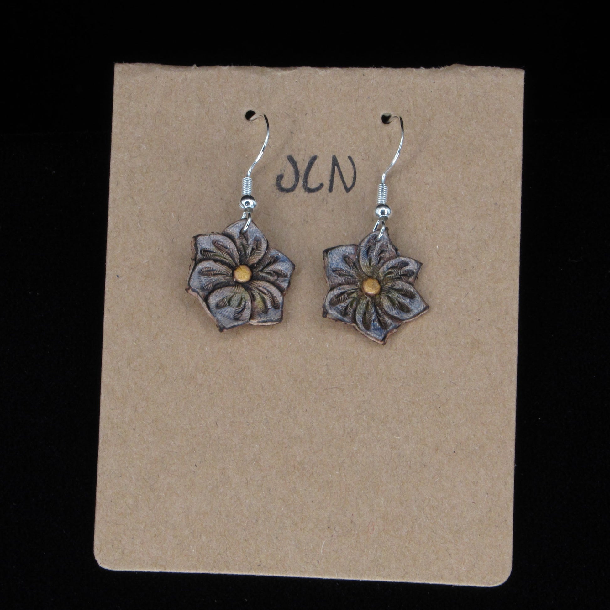 Flower-shaped earrings on a brown card with 'JLN' branding against a black background