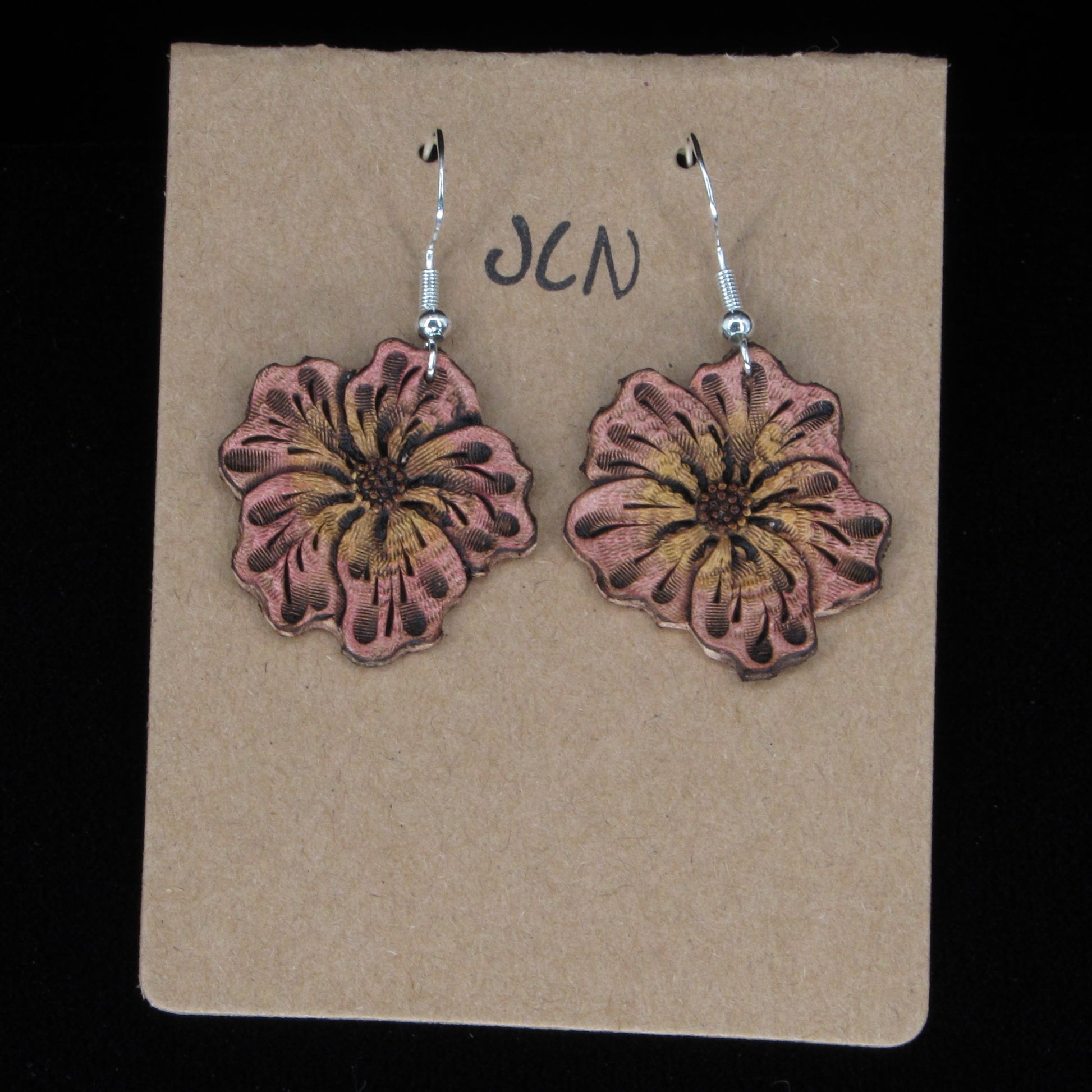 Flower-shaped leather earrings on a brown card with 'JLN' branding against a black background
