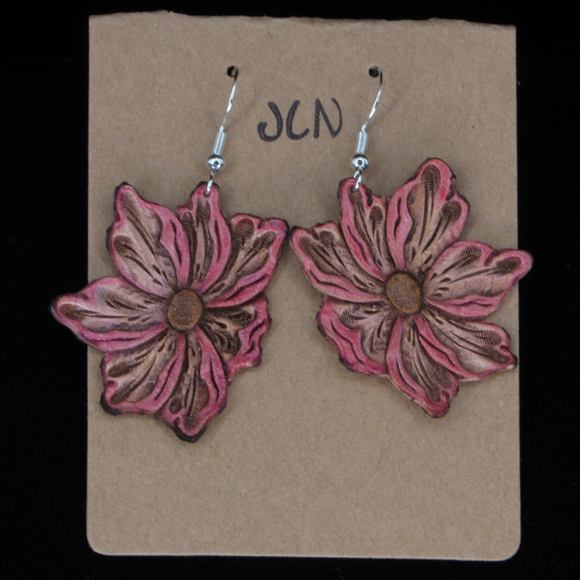 Flower-shaped leather earrings on a brown card with 'JLN' branding against a black background