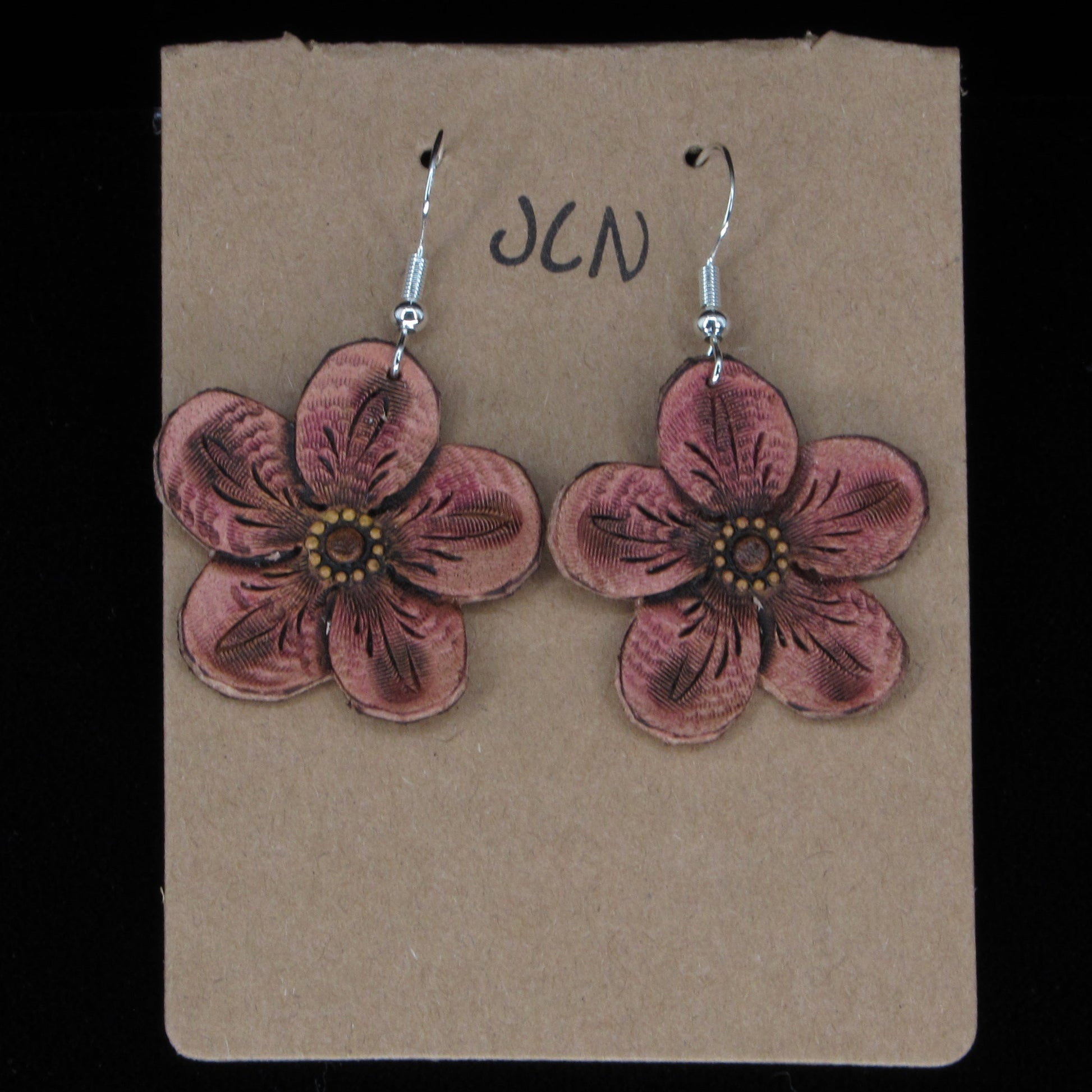 Flower-shaped leather earrings on a brown card with 'JLN' branding against a black background