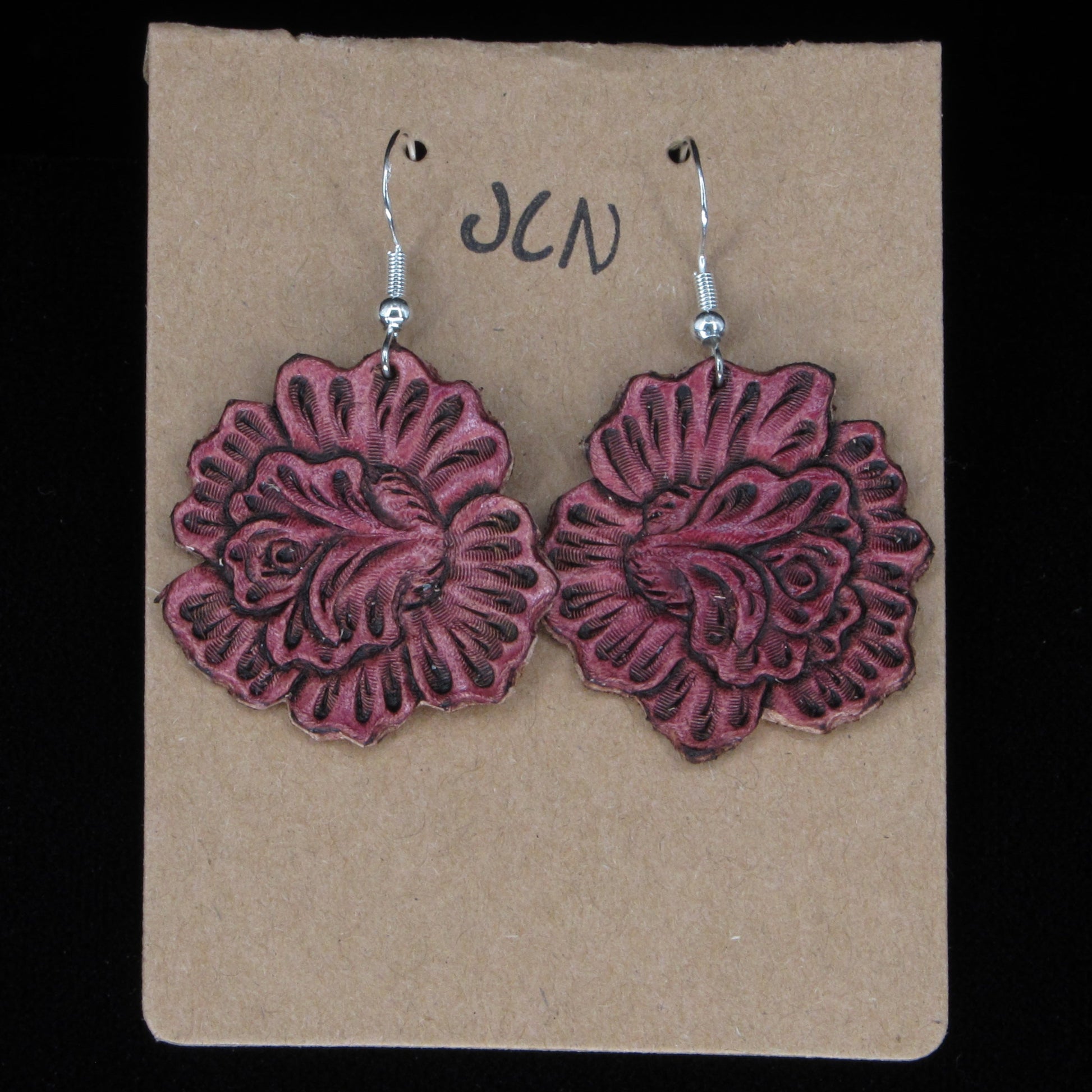 Pink flower-shaped earrings on a beige card with 'JLN' branding against a black background