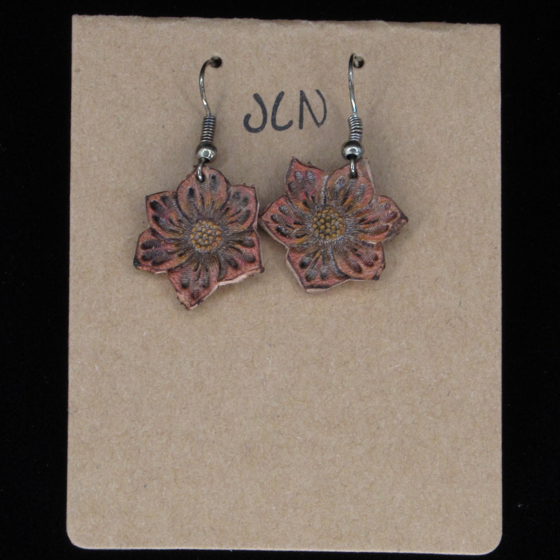 Flower-shaped earrings on a beige card with 'JLN' branding against a black background