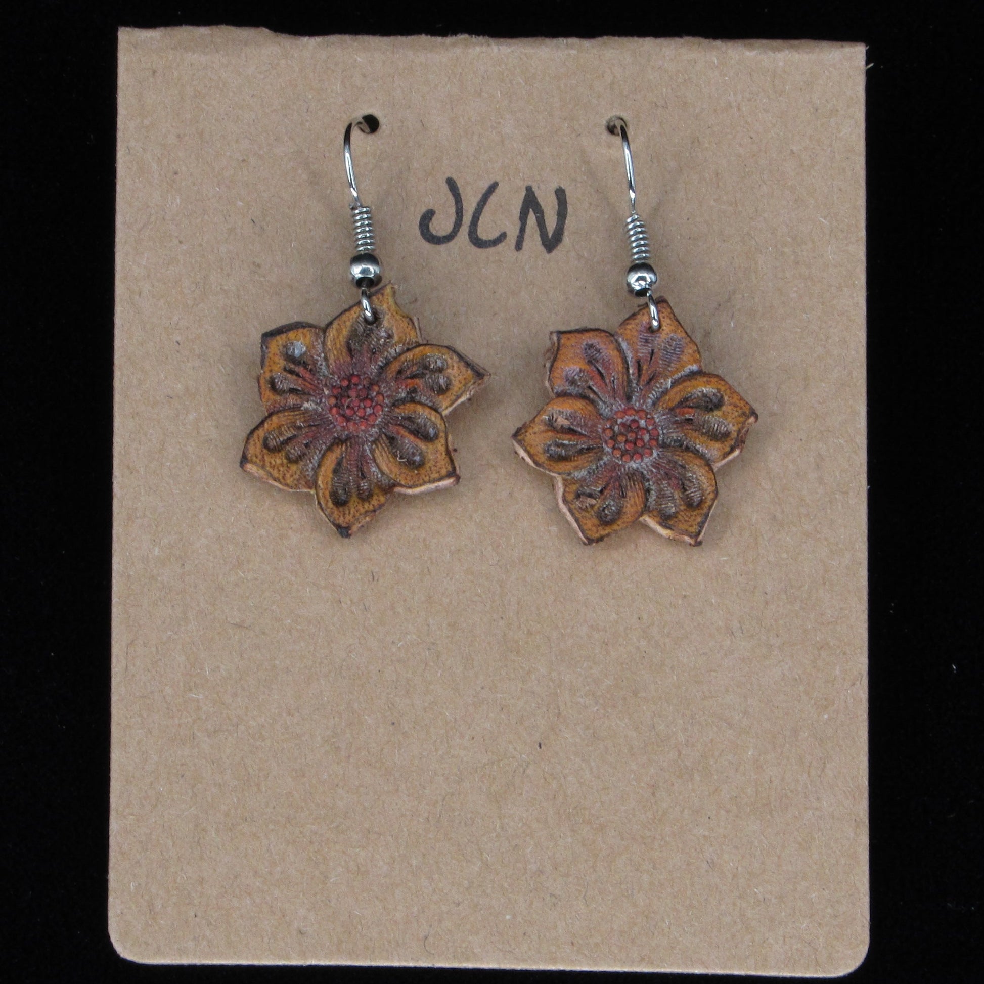 Flower-shaped earrings on a beige card with 'JLN' branding against a black background