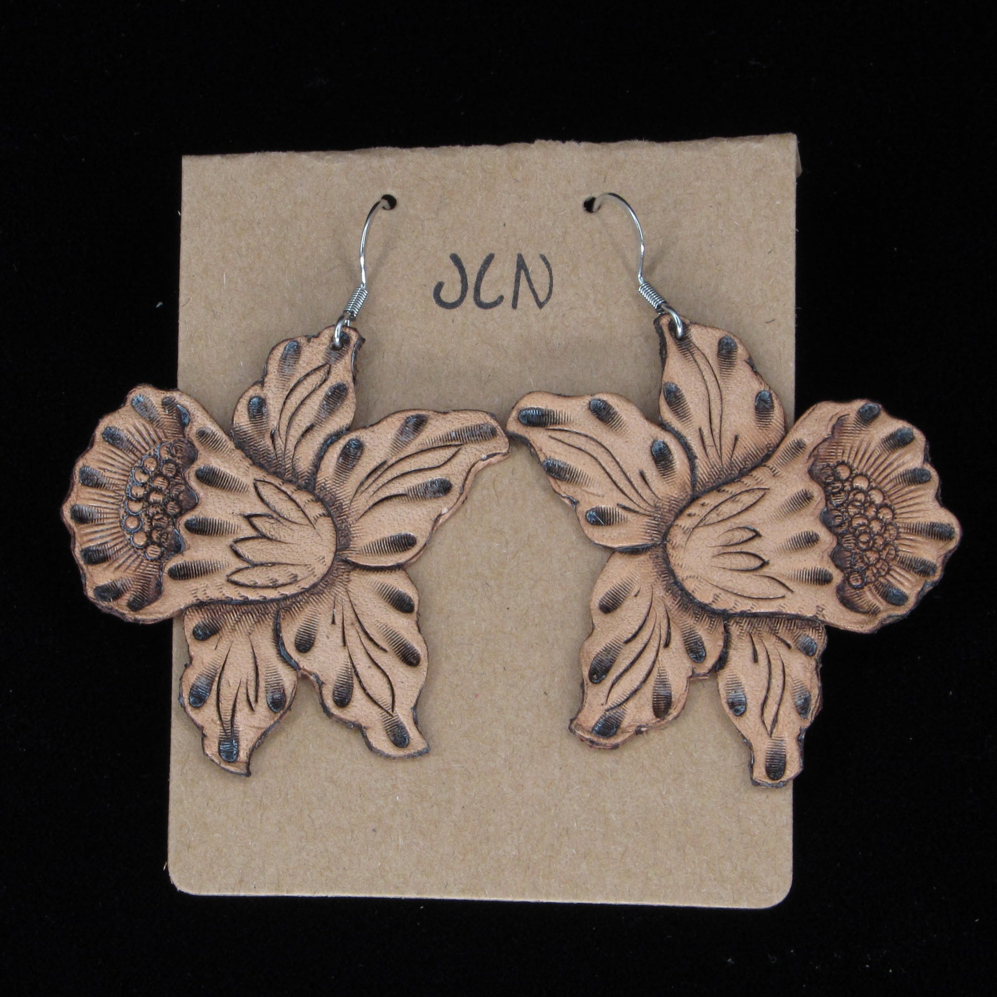 Flower-shaped earrings on a beige card with 'JLN' branding against a black background