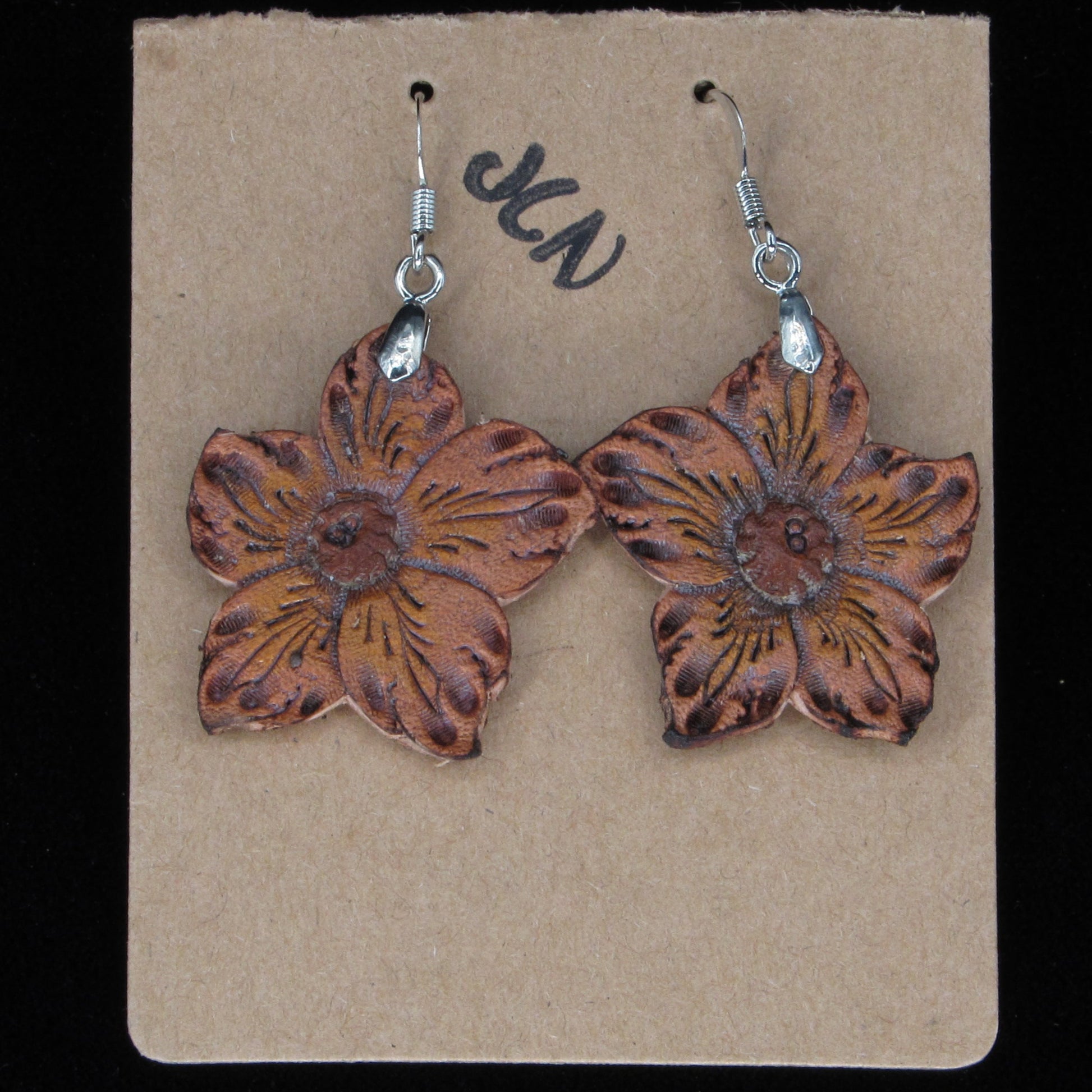 Flower-shaped earrings on a beige card with 'JLN' branding against a black background