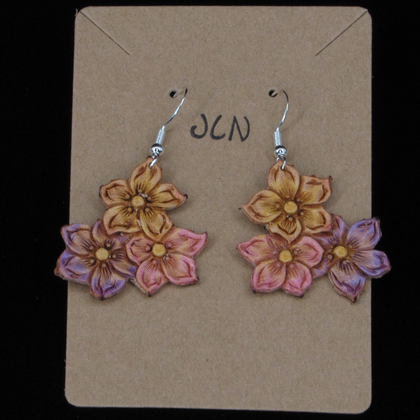 flower shaped leather earrings on a tan card against a black background
