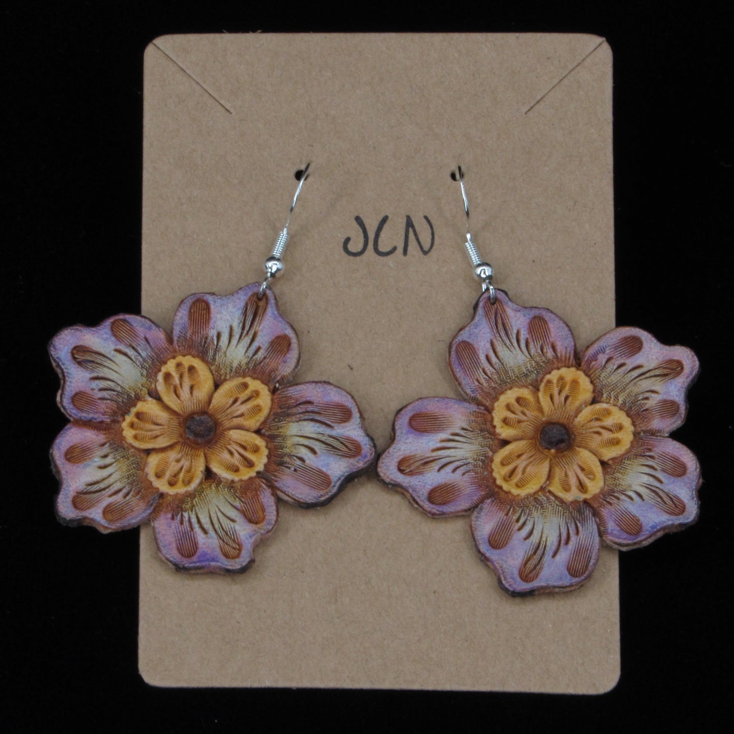 flower shaped leather earrings on a tan card against a black background