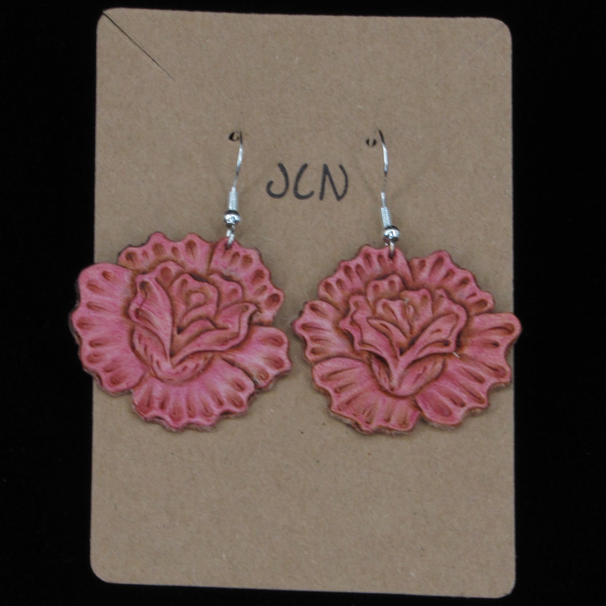 Rose shaped leather earrings on a tan card against a black background