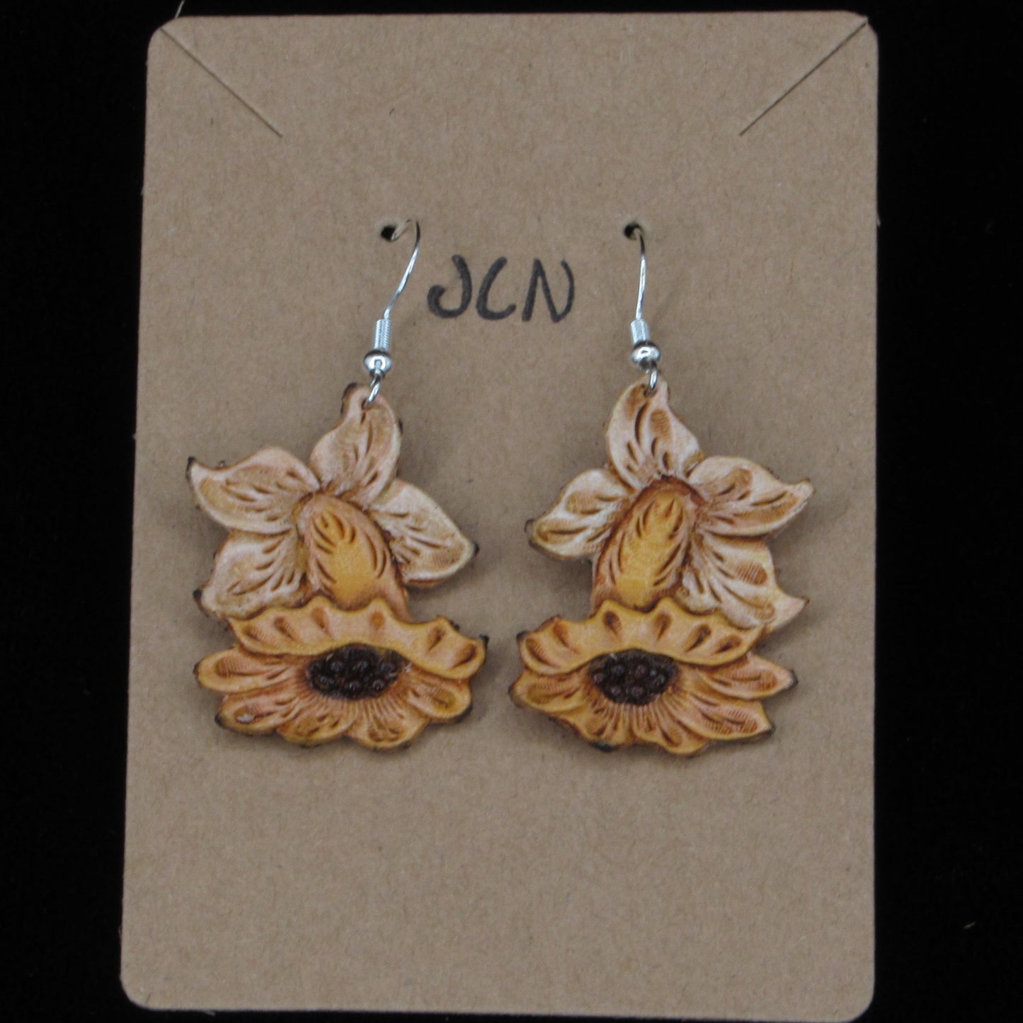 Flower shaped leather earrings on a tan card against a black background