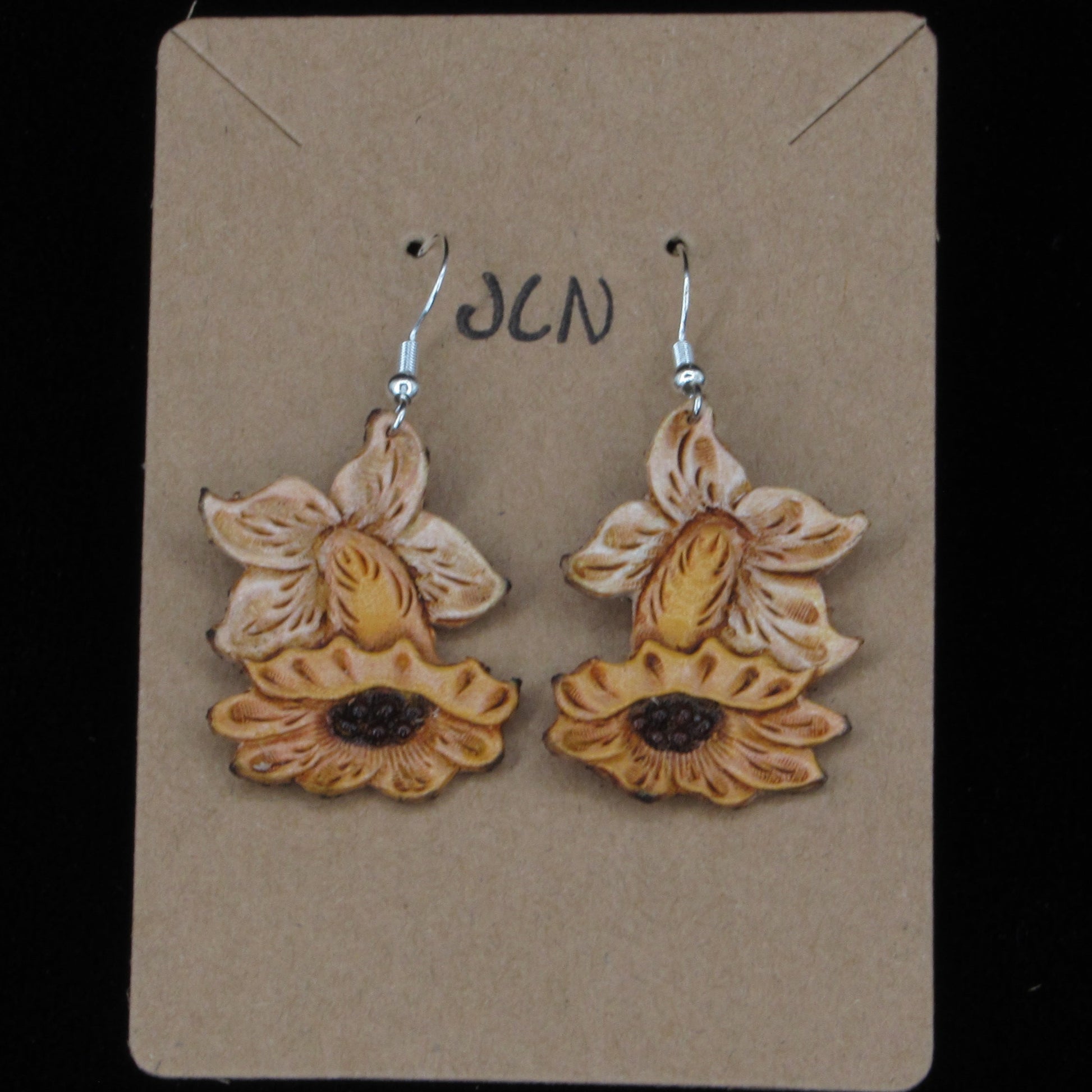 Flower shaped leather earrings on a tan card against a black background