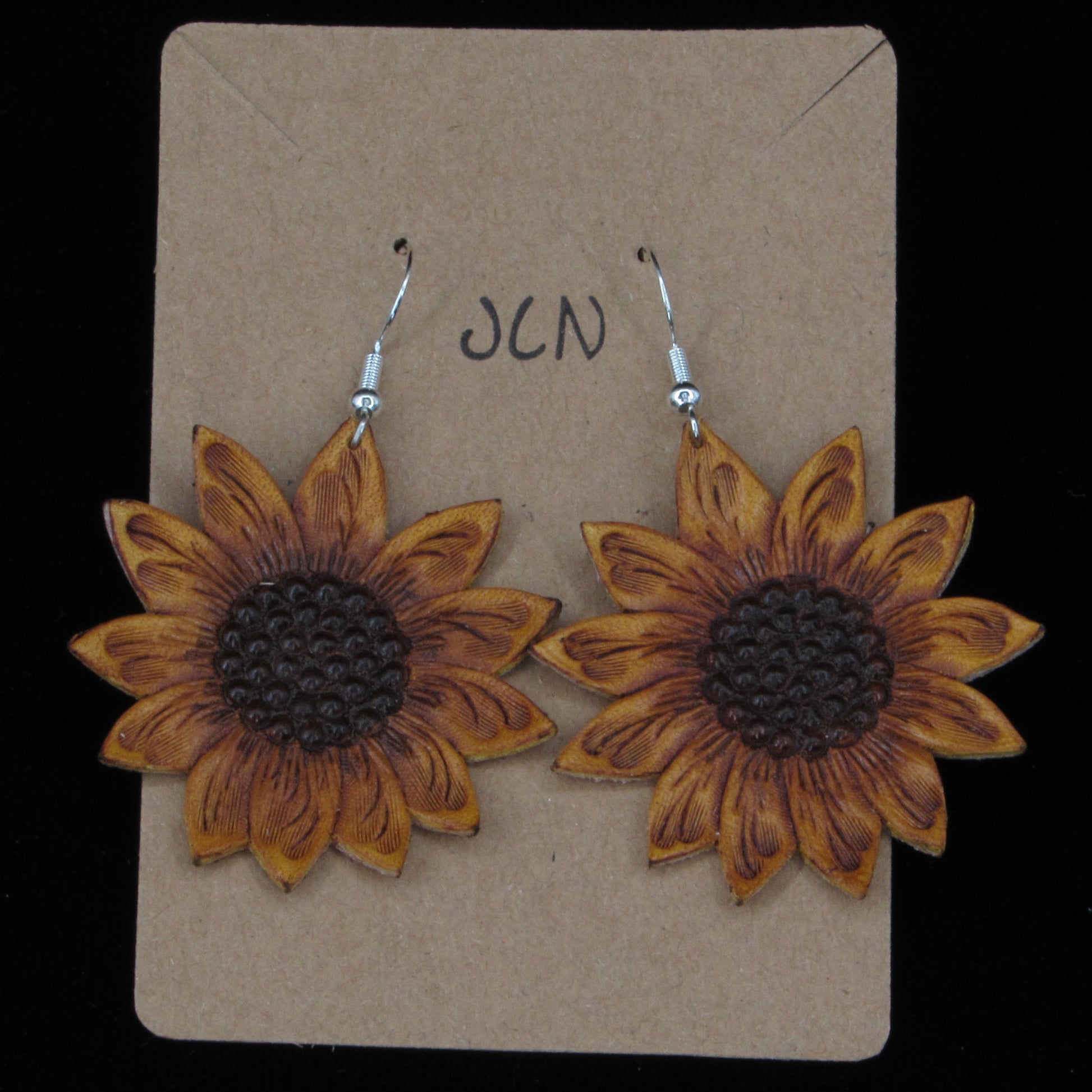 
sunflower shaped leather earrings on a tan card against a back background