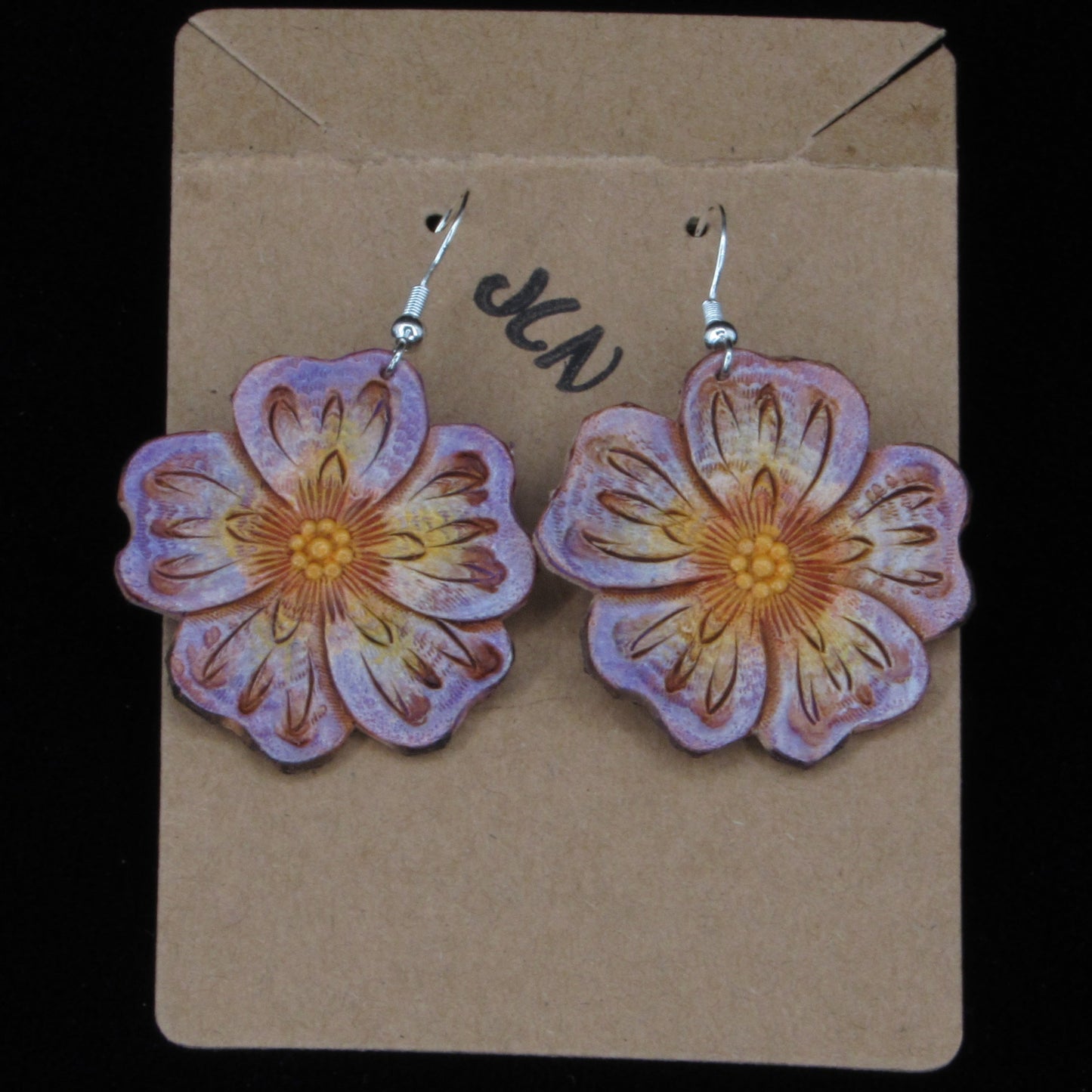 Flower-shaped leather earrings on a cardboard backing with a black background