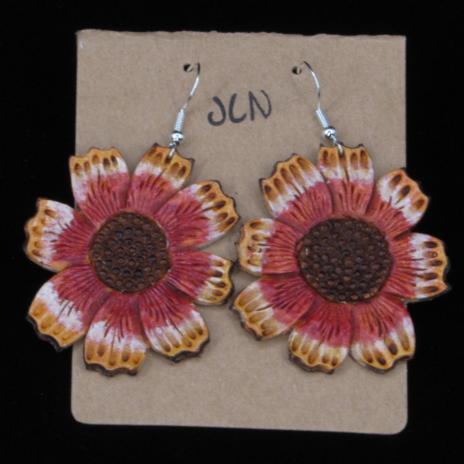 Flower-shaped leather earrings on a cardboard backing with a black background