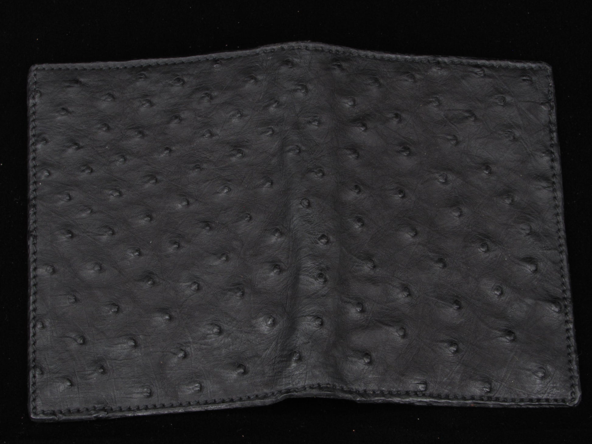 Black ostrich leather passport wallet on a black background