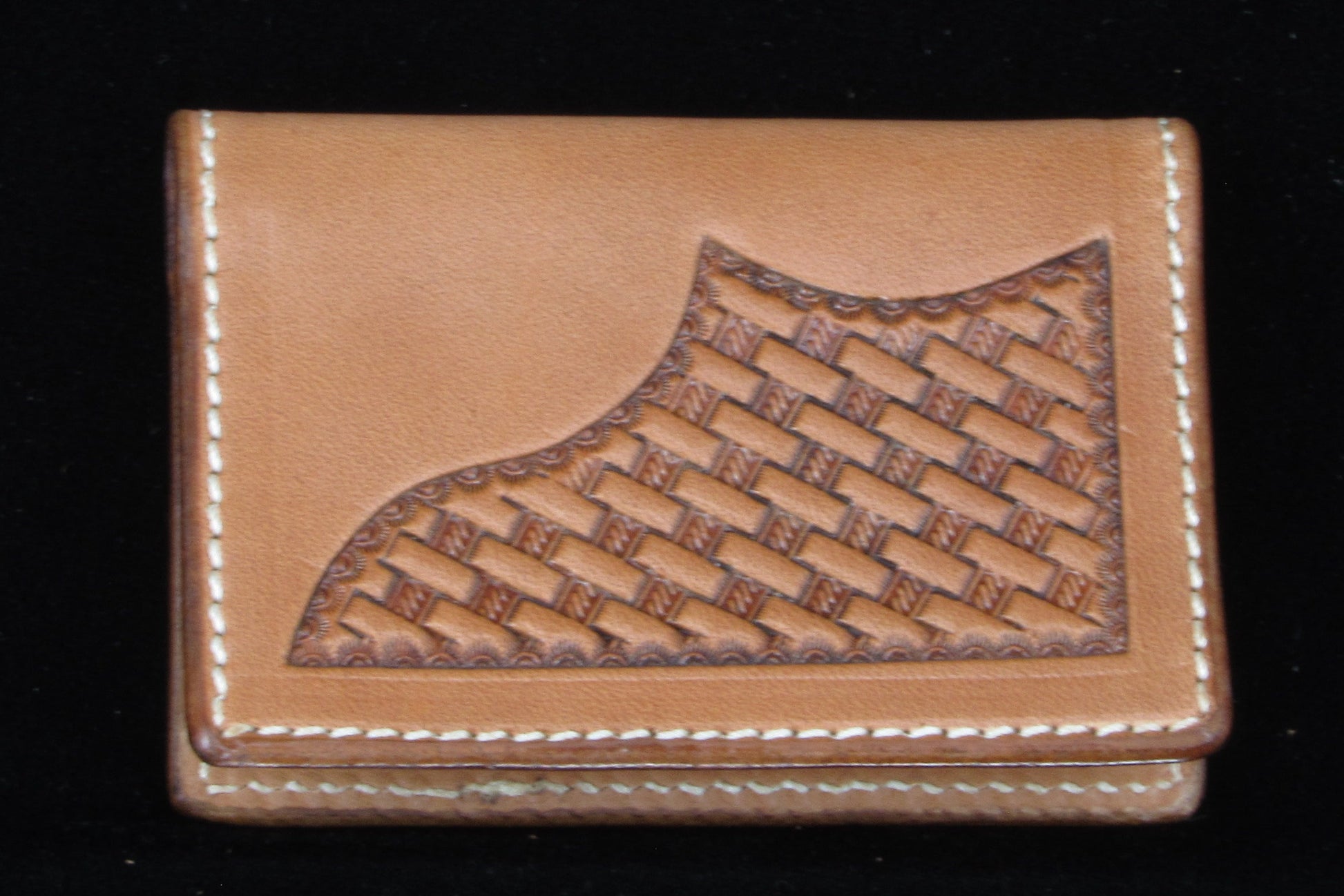 Brown leather wallet with basket stamped corner design on a black background