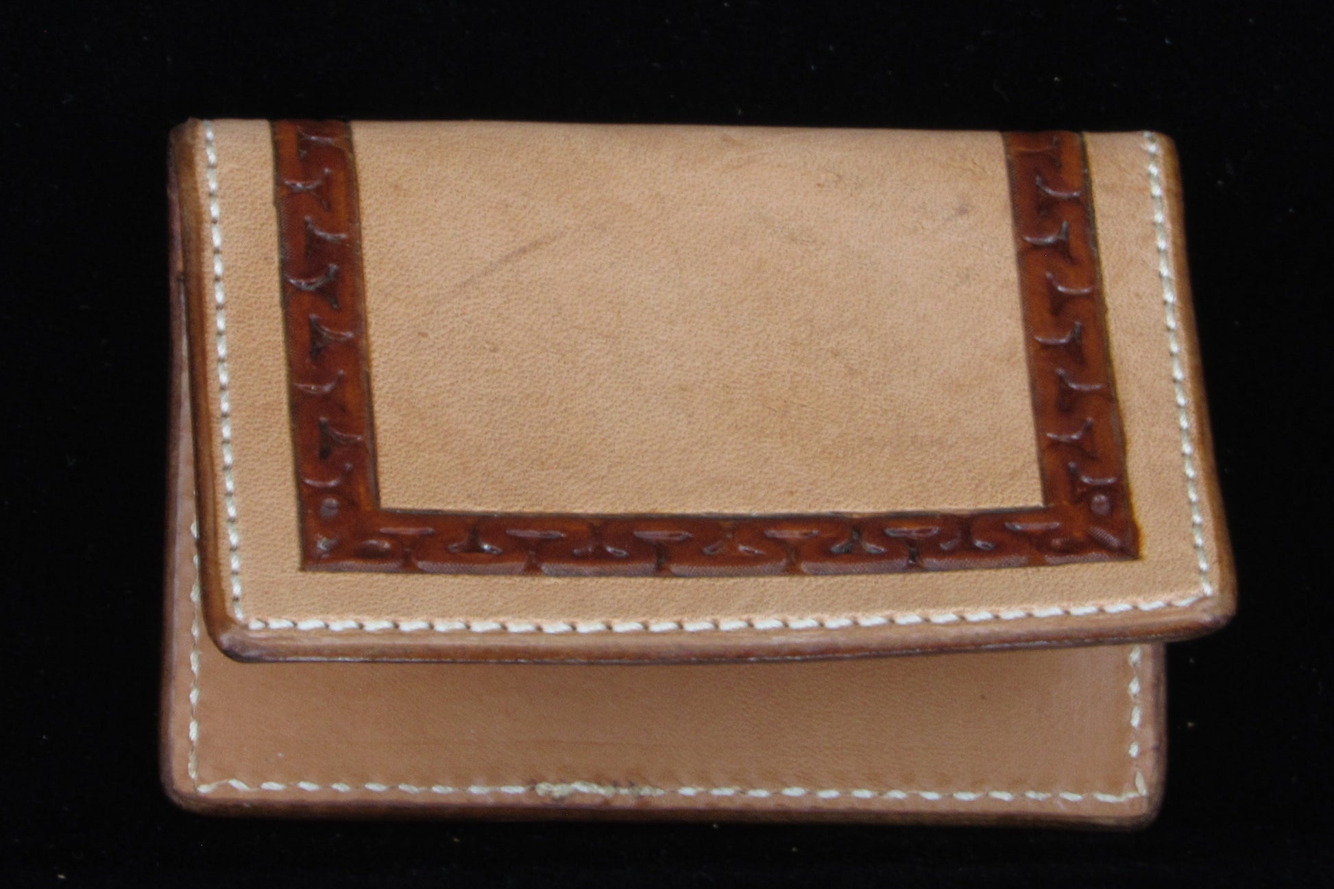 Small leather wallet with decorative border on a black background