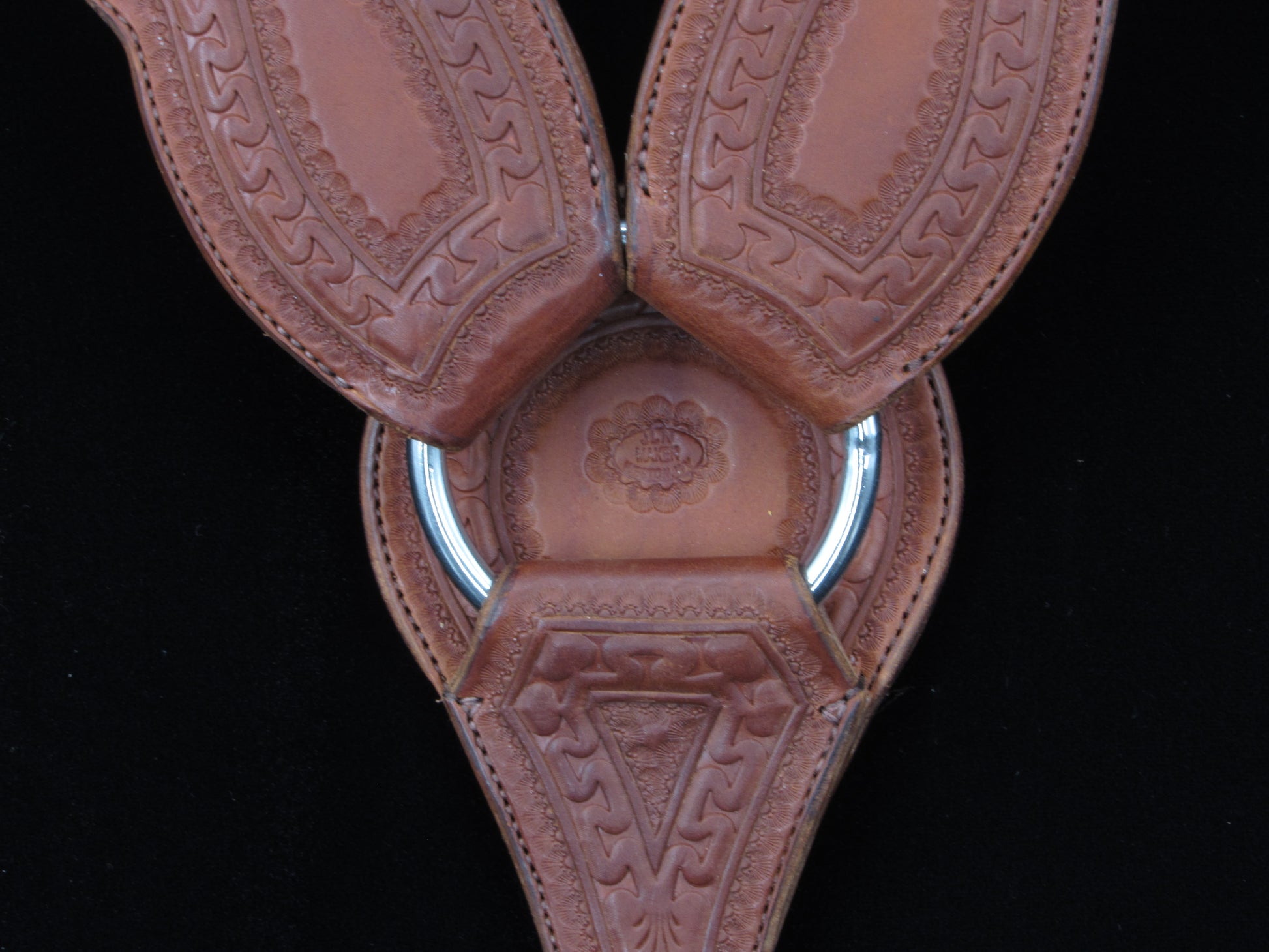 Close-up of a brown leather saddle breastcollar with intricate patterns on a black background